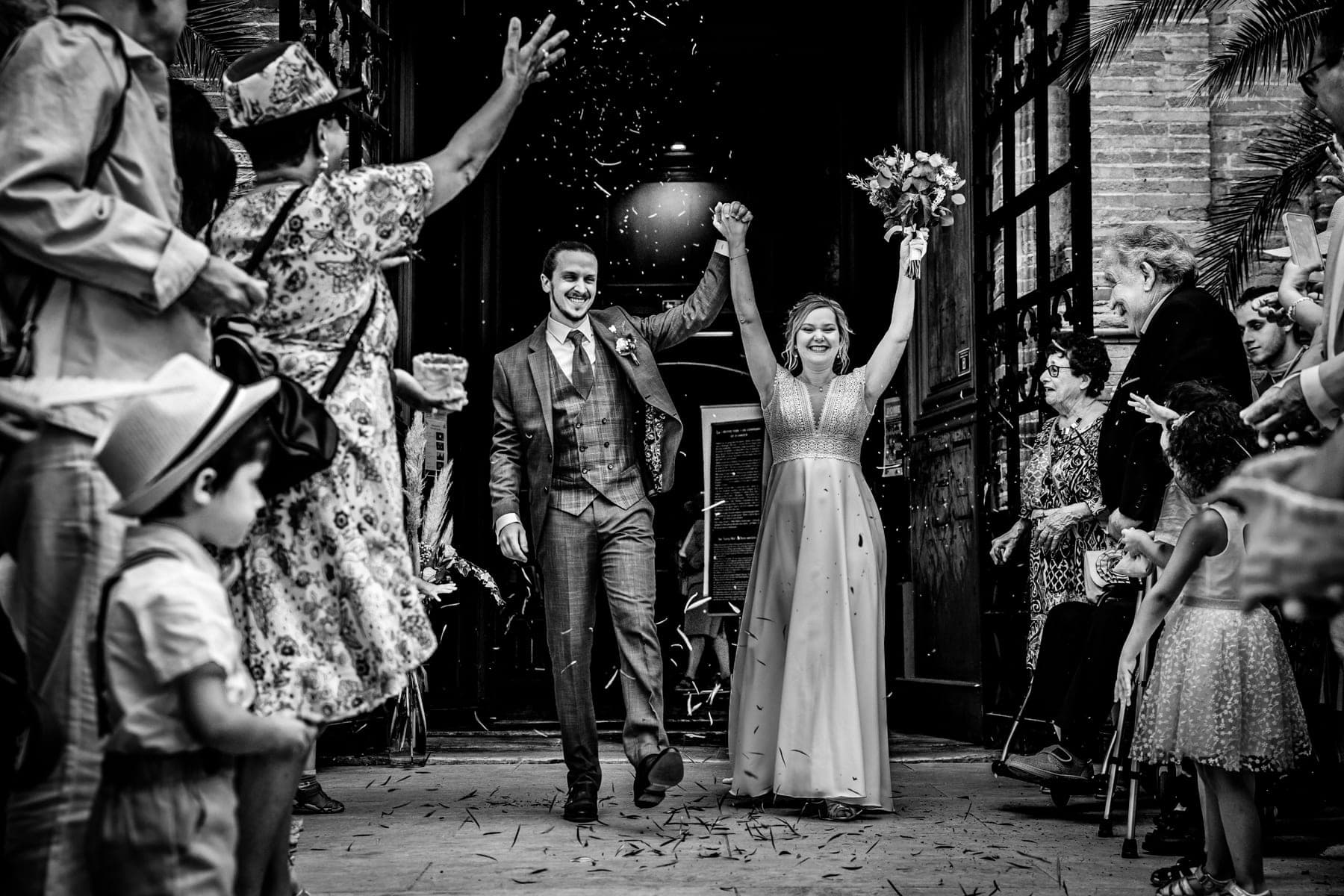 Mariés bras levés à la sortie de l'église sous les confettis — photographe mariage Montauban