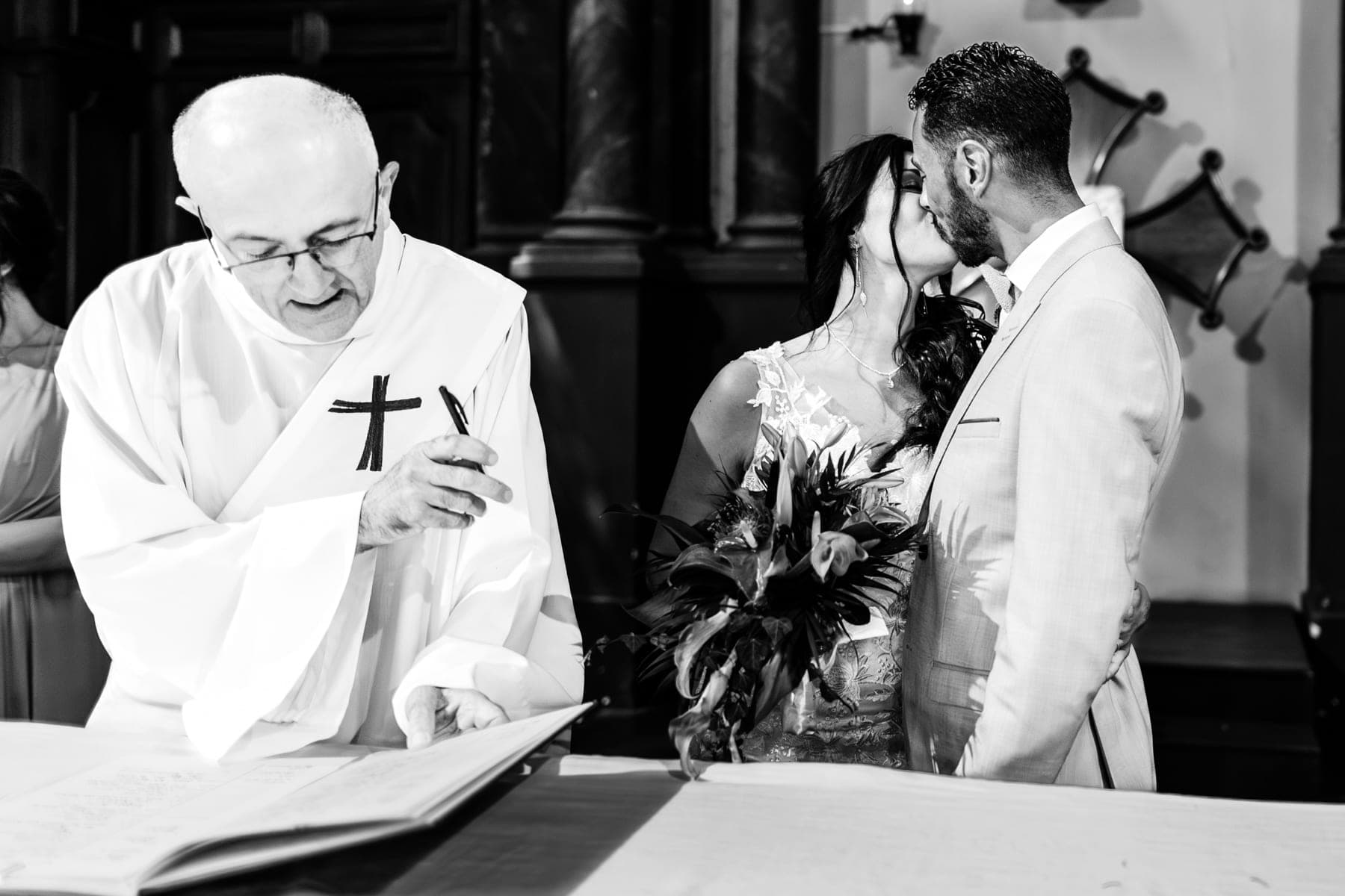Couple qui s'embrasse à l'église pendant la cérémonie sous le regard amusé du prêtre — photographe mariage Montauban