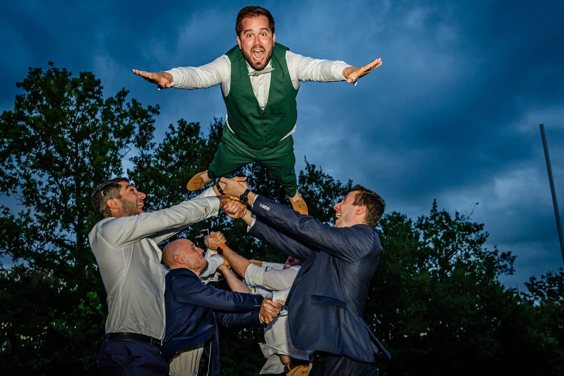 Marié projeté en l'air par ses amis sous un ciel dramatique — photographe mariage Occitanie