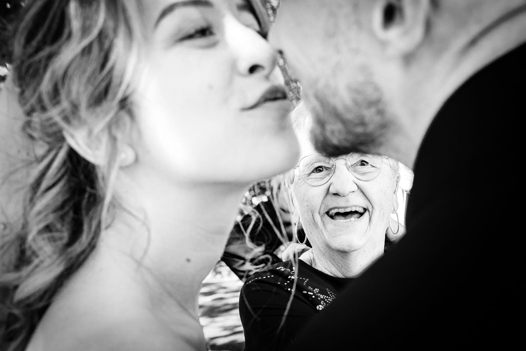 Grand-mère radieuse entre les mariés qui s'embrassent — reportage mariage Montauban