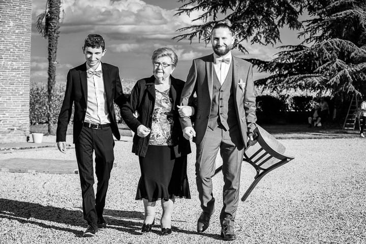 Marche bras dessus bras dessous entre une invitée âgée et deux hommes lors d'un mariage en Occitanie